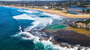 An aerial view of a coastal area with a beach, waves, and a swimming pool. - Beach & Lake Narrabeen Apartment with Outdoor BBQ (Narrabeen)
