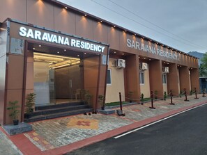 Edificio Saravana Residency con fachada moderna, amplio acceso de vidrio y zona de entrada pavimentada con diseño decorativo.