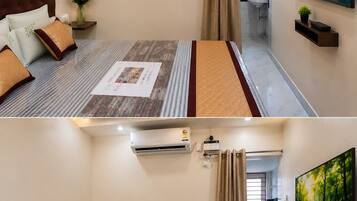 Habitación de hotel con cama, mesita de noche con un jarrón de flores, equipo de aire acondicionado, baño con lavamanos y un cuadro en la pared.