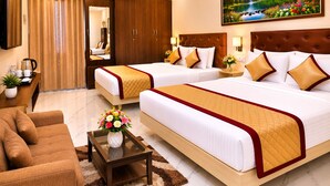 A hotel room with two beds, a sofa, a coffee table with flowers, a TV, and an air conditioning unit. - Saravana Residency  (Periyakulam)
