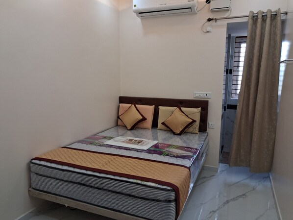 A bedroom with a bed, a headboard, a window with curtains, and an air conditioning unit.