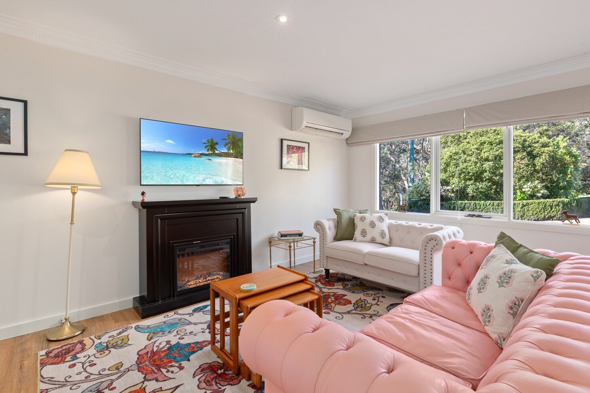 A living room with a fireplace, a sofa, a coffee table, a TV, and a window with a view of trees.