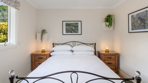 Une chambre à coucher comprenant un lit, deux tables de chevet, une fenêtre avec vue et deux plantes fixées au mur.
