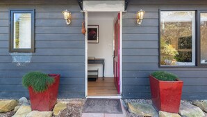 Une maison moderne à l’extérieur sombre, avec un porche bien visible et deux jardinières rouges ornées de plantes vertes.