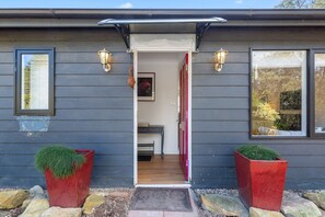 Ein modernes Haus mit dunkler Fassade, einem sichtbaren Eingangsbereich und zwei roten Pflanzgefäßen mit Grünpflanzen.