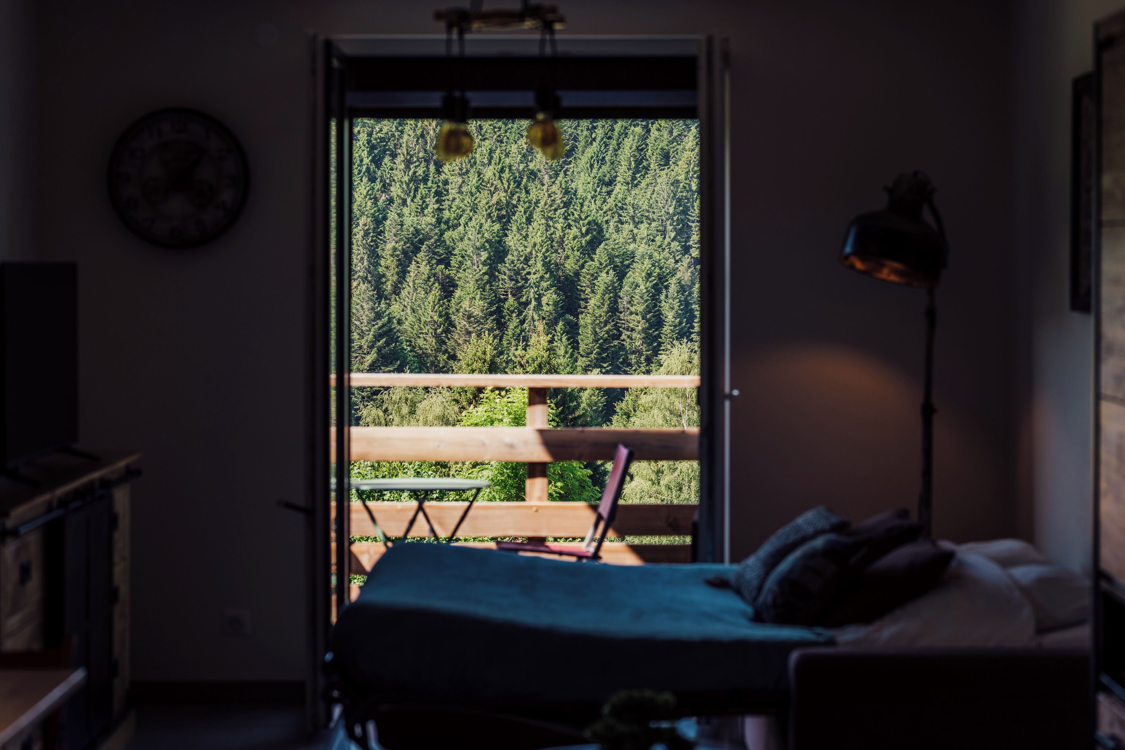 A bedroom with a bed, a desk, and a chair. There is a window with a view of trees.