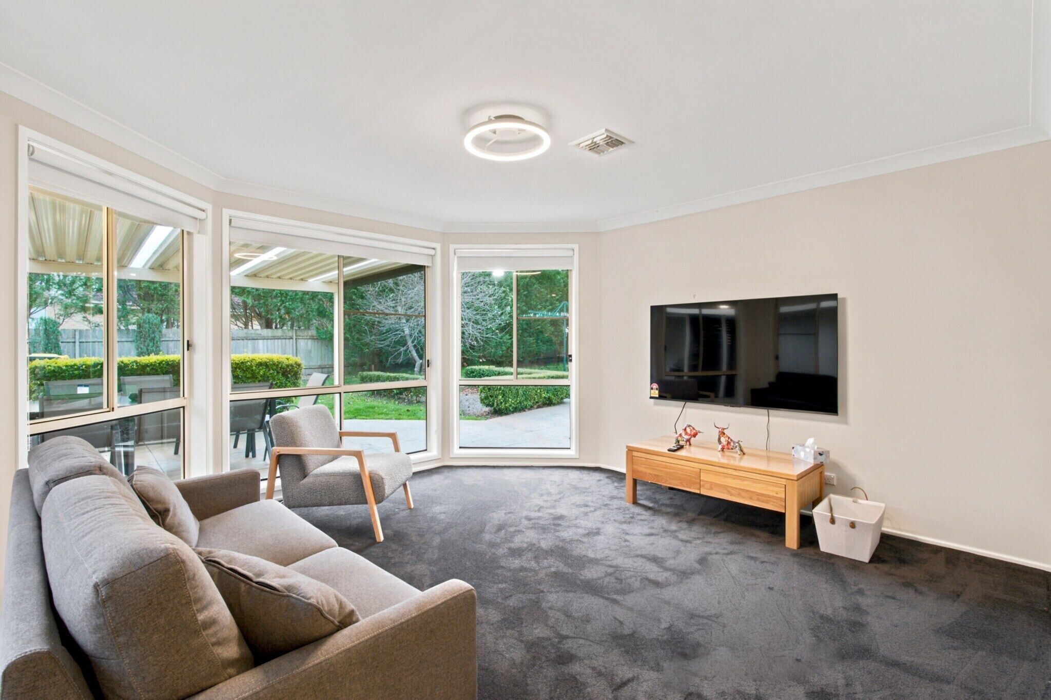 A modern living room with a grey sofa, a wooden side table, and a flat-screen TV mounted on the wall.