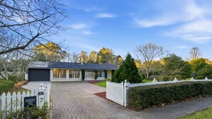 A residential house with a paved driveway, a white picket fence, and a well-maintained garden. - Casa Cypress, Home Near Bowral with Garden and BBQ (Bowral)