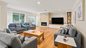 A modern living room with a fireplace, a flat-screen TV, and a stone accent wall. - Casa Cypress, Home Near Bowral with Garden and BBQ (Bowral)