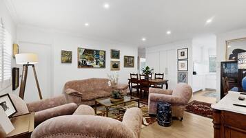A spacious living room with a sofa set, a dining table, and various framed artworks on the walls.