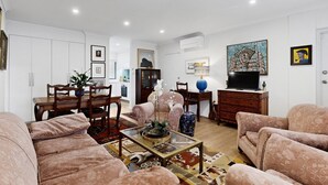A modern living room with a dining area, a sofa set, a coffee table with decorative items, and a TV. - Balcony 2-Bed Apartment in Ashgrove (Ashgrove)