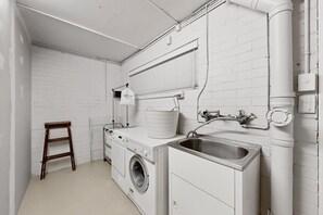 A laundry room with a washing machine, a dryer, a sink, and a wooden stool.