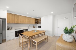 A modern kitchen with wooden cabinets, a dining table with chairs, and a refrigerator. - Poolside 2-Bed Apartment at Lake Kawana (Birtinya)