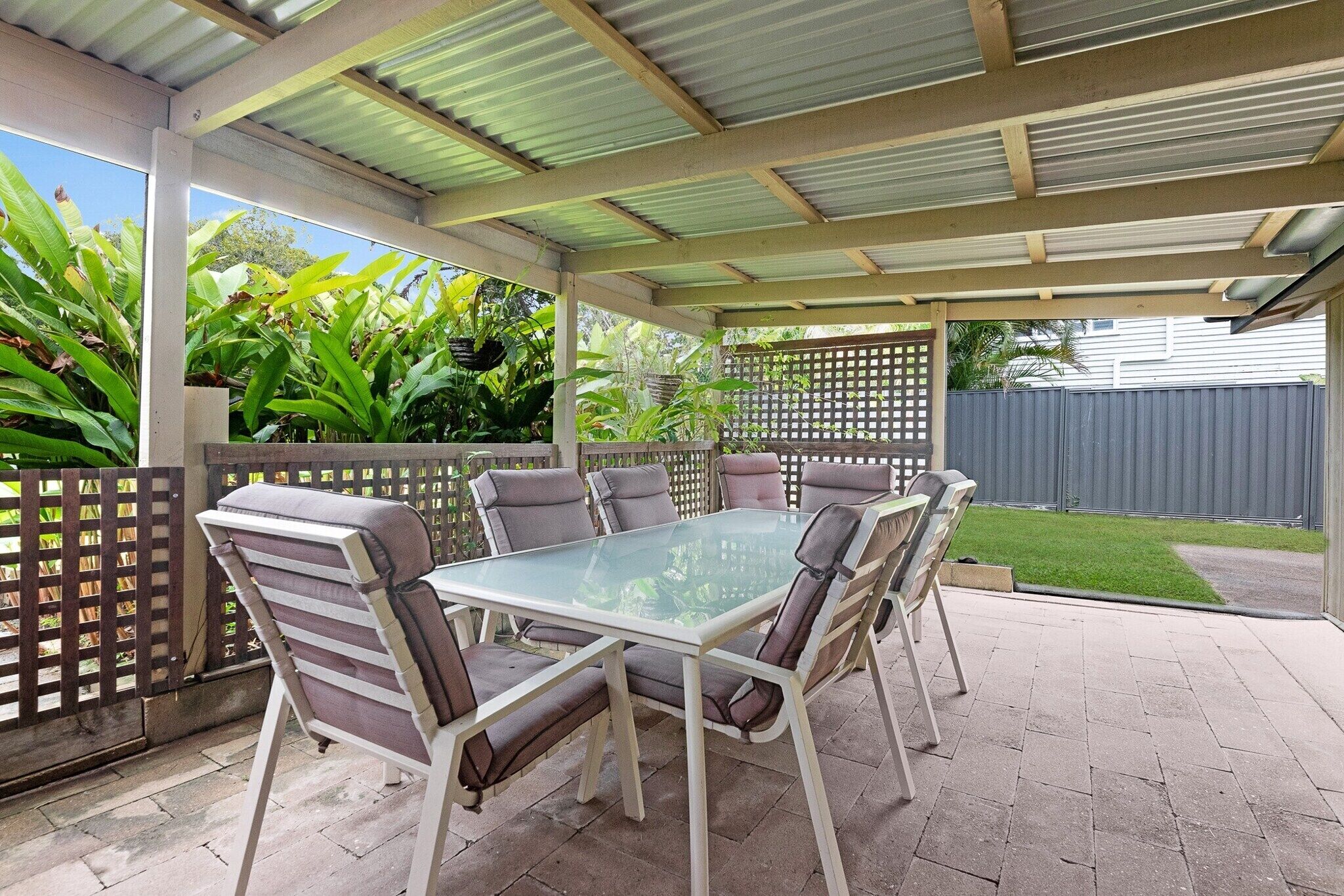 Une terrasse extérieure avec une table à plateau en verre et six chaises.