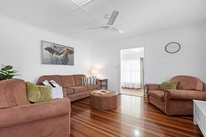 A spacious living room with a brown sofa set, a round ottoman, a ceiling fan, and a painting on the wall. - Two Bed Terrace Near Hervey Bay Beaches (Torquay)