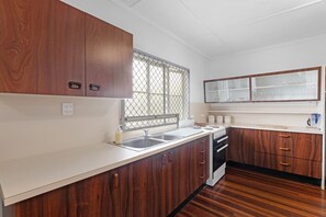 A kitchen with wooden cabinets, a window with a metal screen, a sink, and a stove. - Two Bed Terrace Near Hervey Bay Beaches (Torquay)
