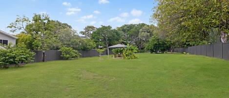 A backyard with a grassy lawn, a wooden fence, and a covered patio area.