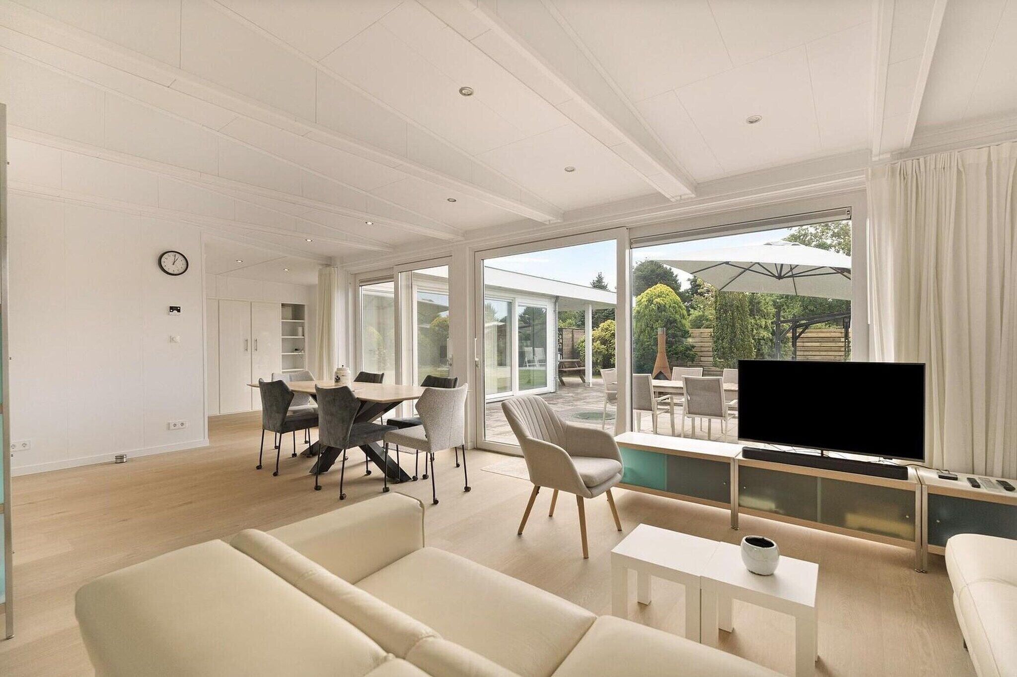 A modern living room with a flat-screen TV, a sofa, and a dining area with chairs and a table.