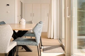 Ein stilvoller Essbereich mit einem Holztisch und grau gepolsterten Stühlen, einem weißen Schrank im Hintergrund und einer Glastür, die nach draußen führt.