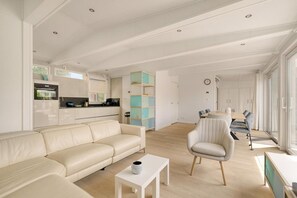 Ein modernes Wohnzimmer mit einer Couch, einem Essbereich mit Tisch und Stühlen sowie einer Küche mit Geräte.
