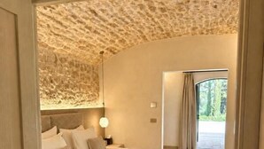 A bedroom with a large bed, a nightstand, a lamp, and a view of the outdoors through a window. - Tenuta Legaro (Monopoli)