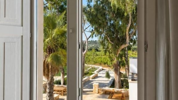 An open door leading to an outdoor patio with a table and chairs, surrounded by trees and a clear sky. - Tenuta Legaro (Monopoli)
