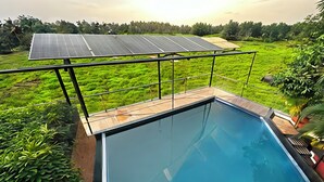 En swimmingpool med utsikt över solpaneler och frodig grönska.