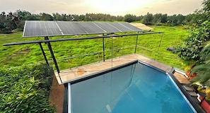 Piscina con vistas a paneles solares y abundante vegetación.
