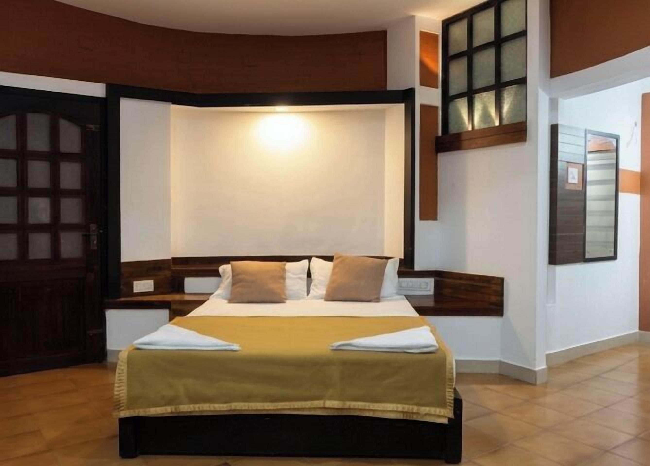A hotel room with a bed, bedside tables, a nightstand, and a window with blinds.