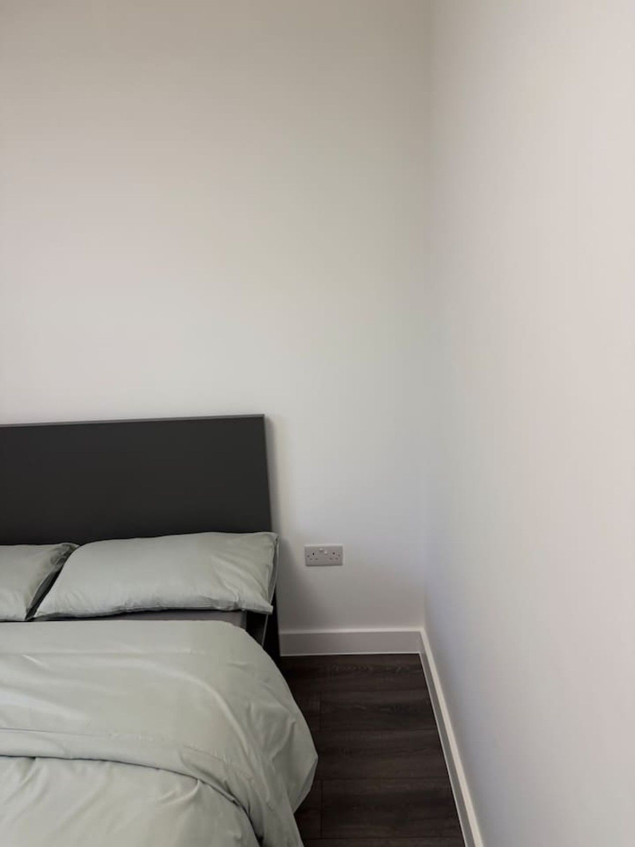 Een slaapkamer met een bed, een donker hoofdeinde en een witte muur.