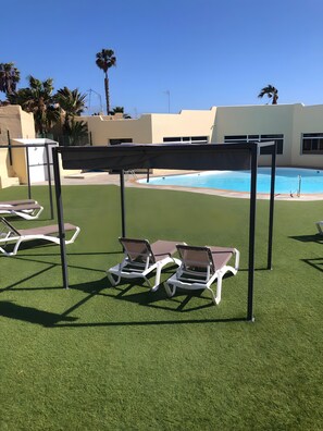 Zona de piscina amb gespa artificial, gandules i una estructura de pèrgola.