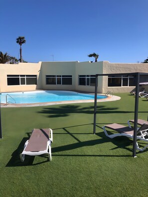 Uma área de piscina com grama sintética, espreguiçadeiras e um edifício com janelas amplas.