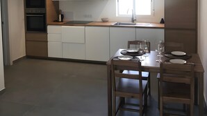 A modern kitchen with white cabinets, a wooden dining table set for four, and a window providing natural light. - Vacation Home 'Casa Del Mar' with Shared Pool, Private Garden and Wi-Fi (Costa Calma)