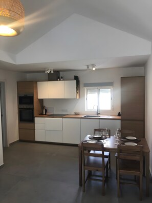 Uma cozinha moderna com armários brancos, uma mesa de jantar de madeira para quatro pessoas e uma janela que oferece luz natural.