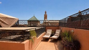 Terraza en la azotea con dos sillones de lounge, una zona cubierta y vistas a un edificio con torre.