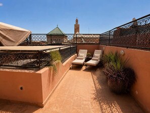 Terraza en la azotea con dos sillones de lounge, una zona cubierta y vistas a un edificio con torre.