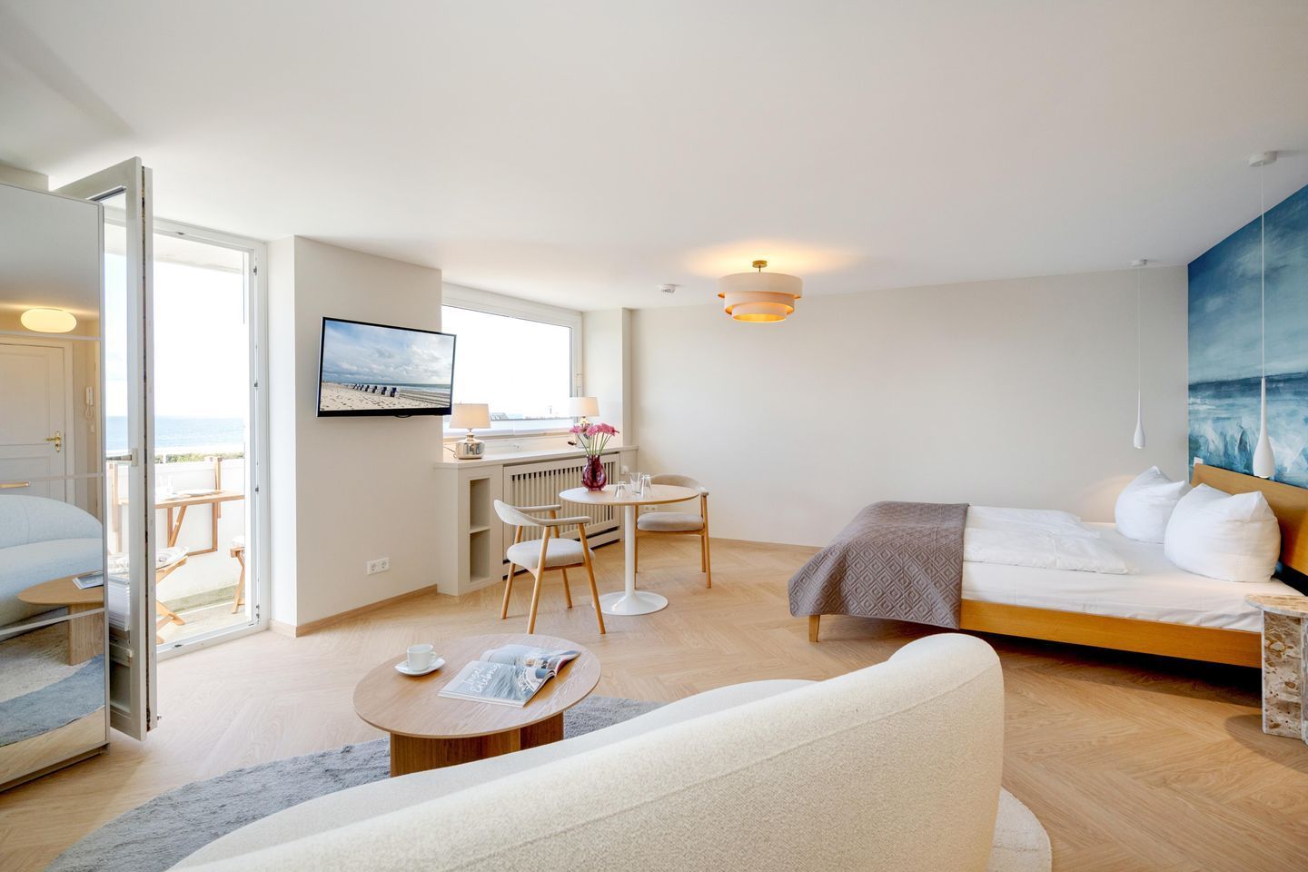 A modern hotel room with a bed, a desk, and a view of the beach.