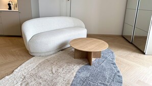 Moderni olohuone, jossa on sohva, pyöreä puinen sohvapöytä ja lattiavalaisin.