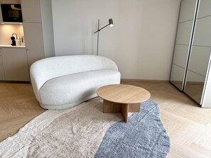 A modern living room with a sofa, a round wooden coffee table, and a floor lamp. - Ocean View - Modern apartment, balcony with ocean view, parking space, Wi-Fi. Pets (Sylt)