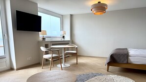 Moderni hotellihuone, jossa on sänky, pyöreä pöytä, kaksi tuolia, televisio ja ikkuna.
