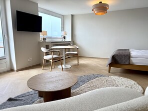 A modern hotel room with a bed, a round table, two chairs, a TV, and a window. - Ocean View - Modern apartment, balcony with ocean view, parking space, Wi-Fi. Pets (Sylt)