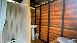 Interior em madeira com chuveiro, pia e vaso sanitário.