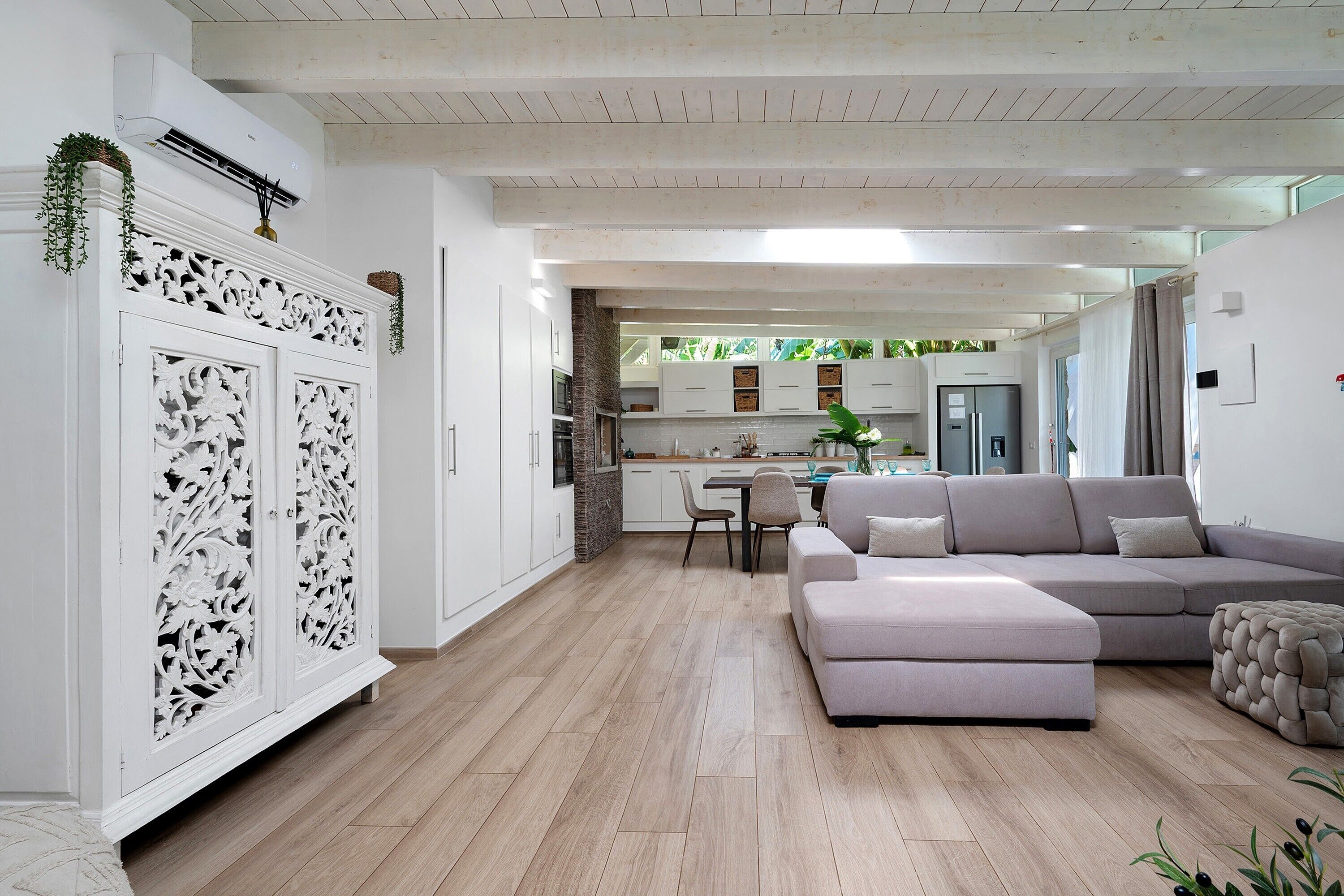 A modern kitchen with white cabinetry, a stone accent wall, and a dining area with a grey sofa and ottoman.