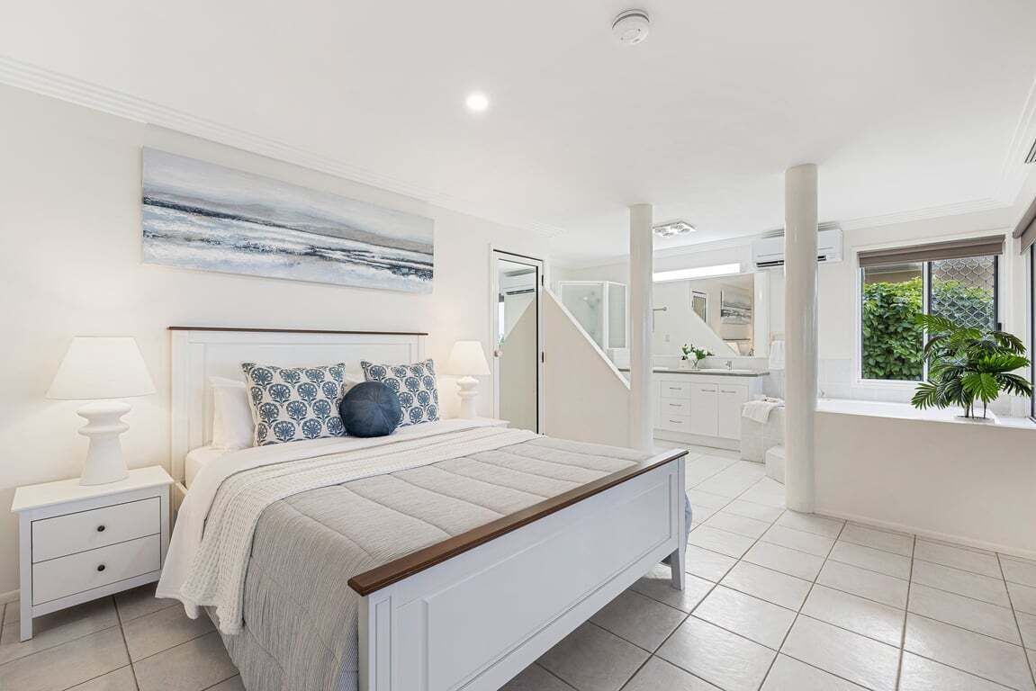 A bedroom with a bed, nightstands, a painting, a staircase, and a bathroom.