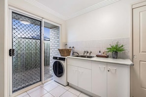 A compact kitchen with a washing machine, a sink, and a potted plant.