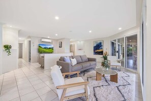 A modern living room with a sofa, armchair, and coffee table, a television, and a large window.
