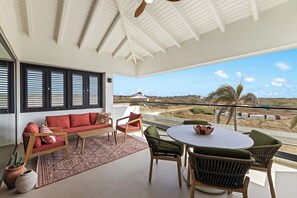 A spacious balcony with a sofa, chairs, and a table, overlooking a scenic landscape. - Moyo Apartment. 2 bedrooms & 2 bathrooms. 15-minute drive to Jan Thiel & Mambo (Willemstad)