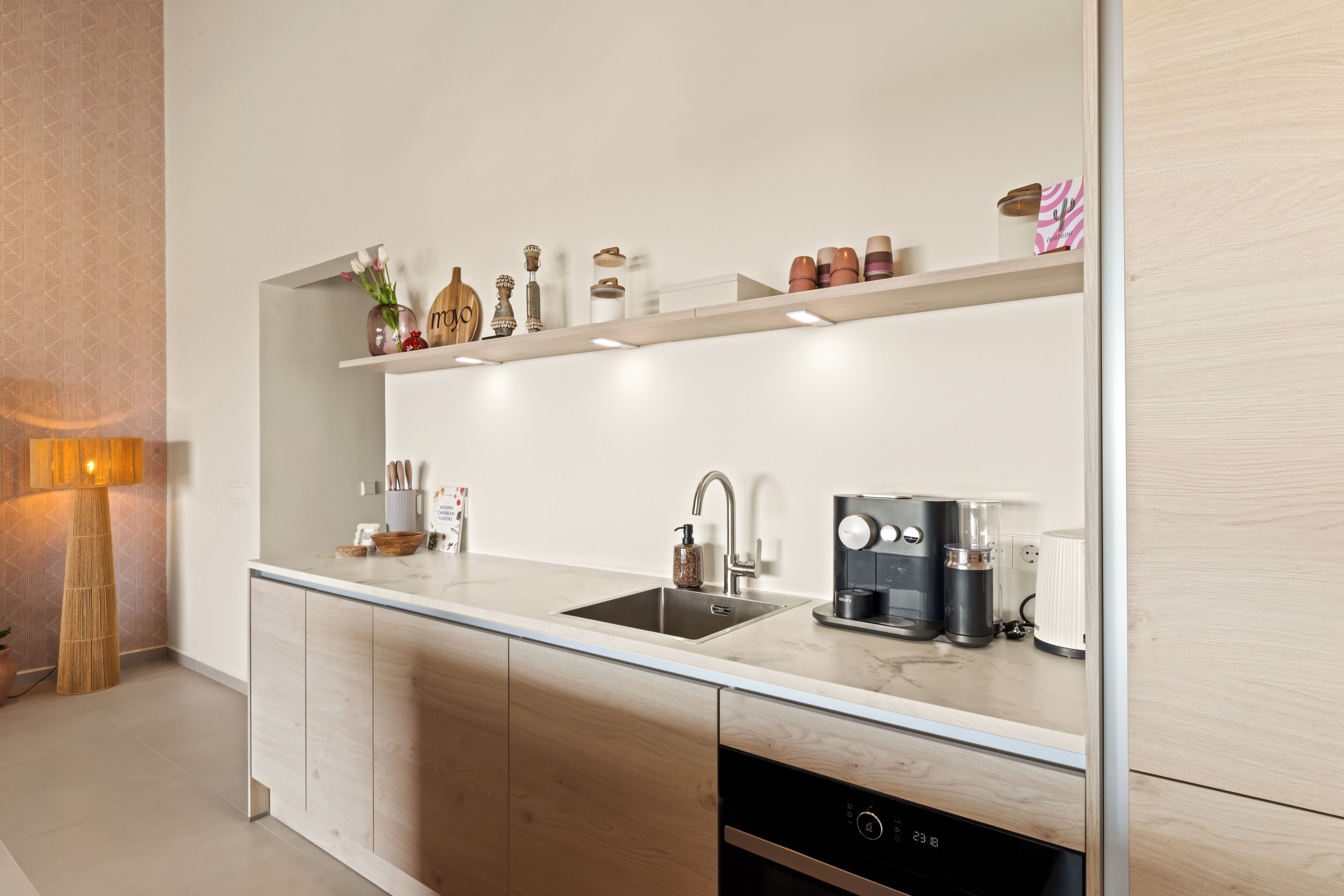 Una cocina moderna con lavavajillas integrado, cafetera y una variedad de utensilios de cocina en estantes abiertos.
