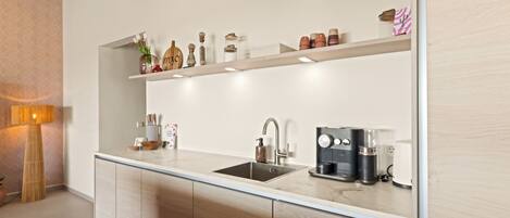 Een moderne keuken met een ingebouwde vaatwasser, een koffieapparaat en diverse keukengerei op open planken.