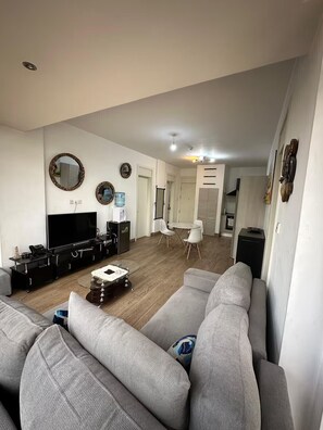 A modern living room with a large grey sofa, a flat-screen TV, and a coffee table. There is a dining area with a white table and chairs. - 2-bedroom apartment in adorable Nairobi with fitness room access (Nairobi)
